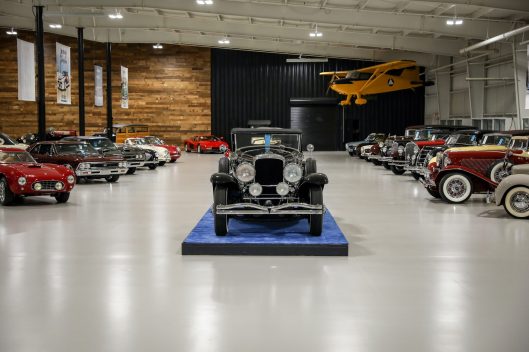 The Auburn Classic Cars showroom with a vintage car on a blue platform beneath a suspended yellow airplane